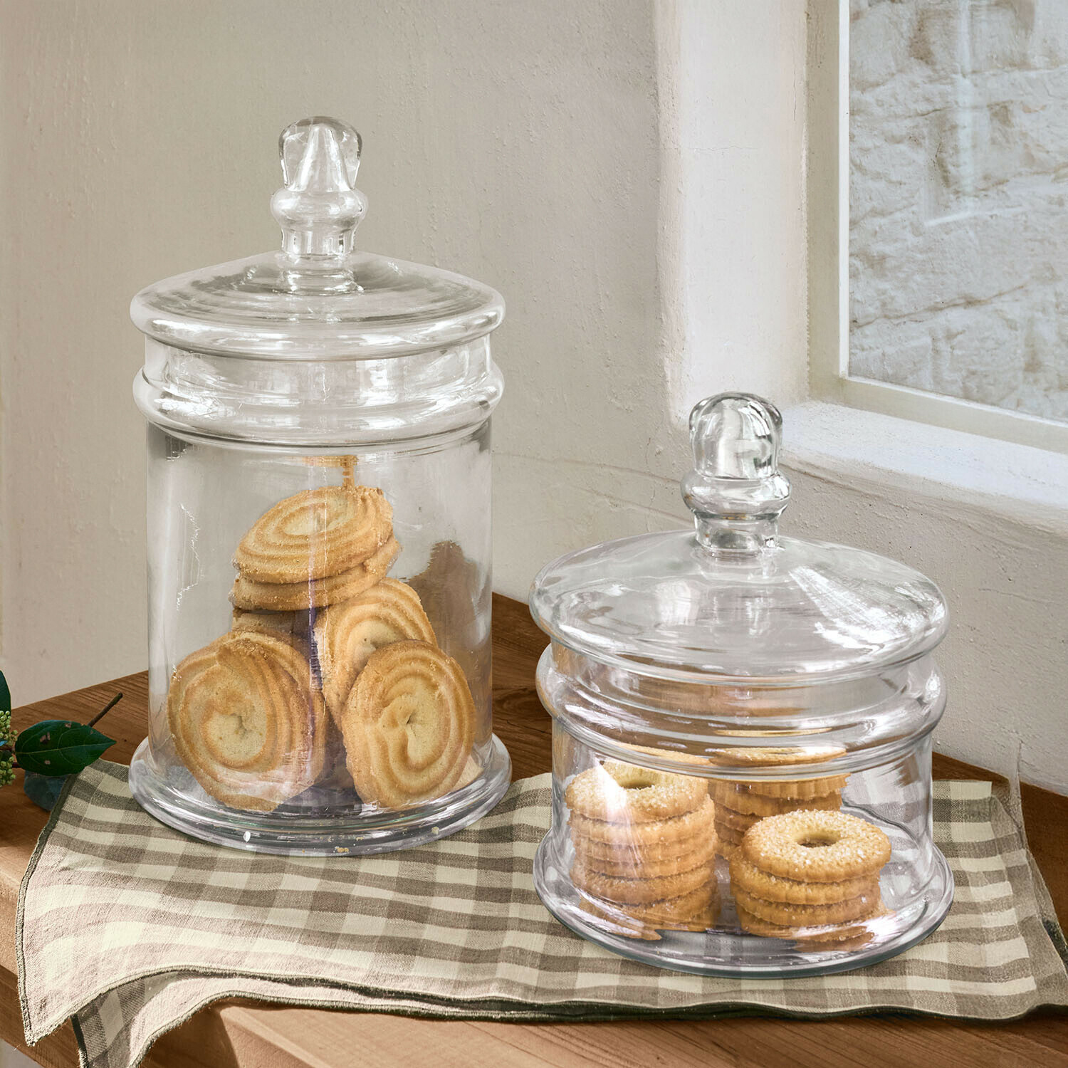 Due barattoli di vetro trasparente con coperchi pieni di biscotti su tavolo di legno con tovaglia a quadri