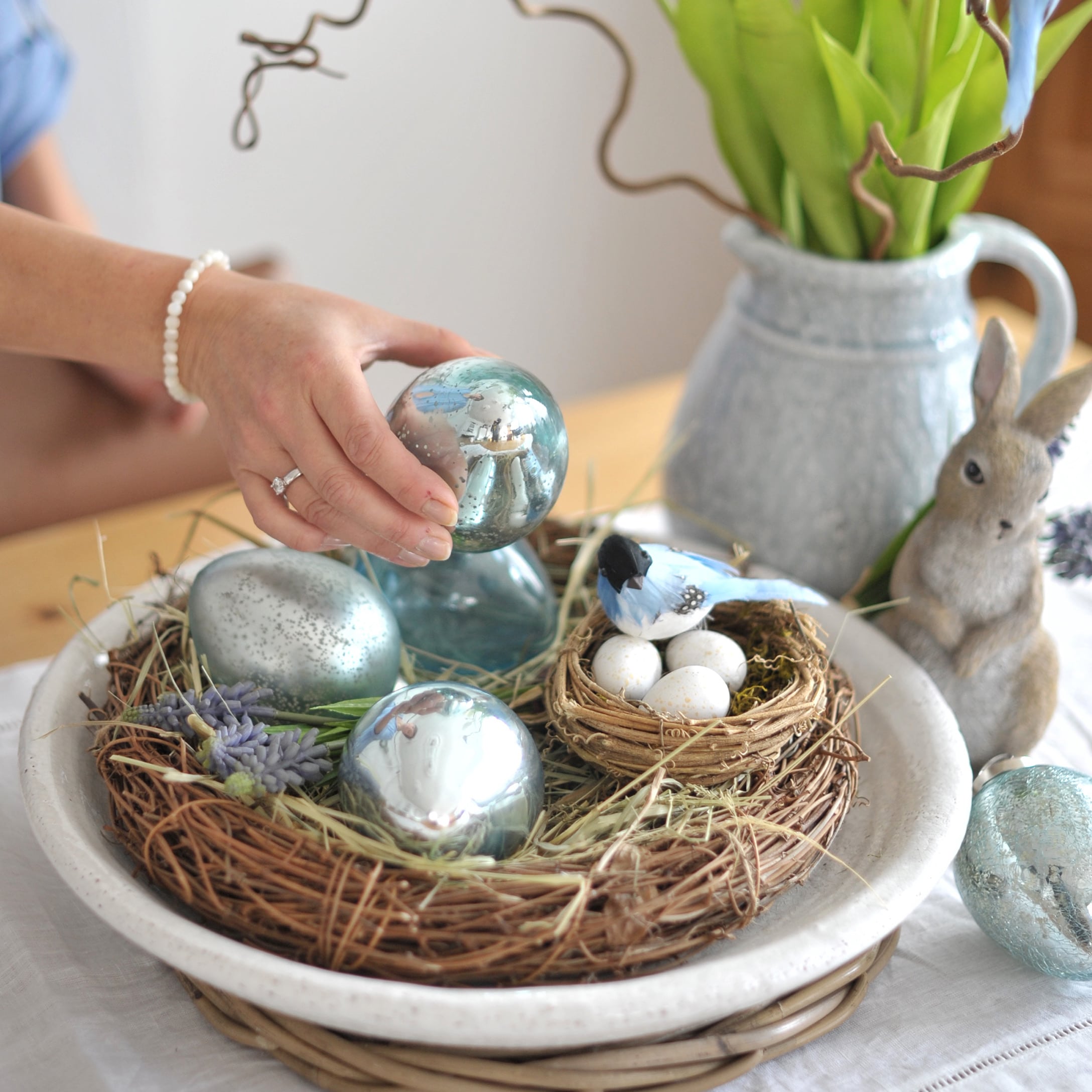 Decorazione pasquale con uova di vetro blu e nido con uova bianche su tavolo in legno