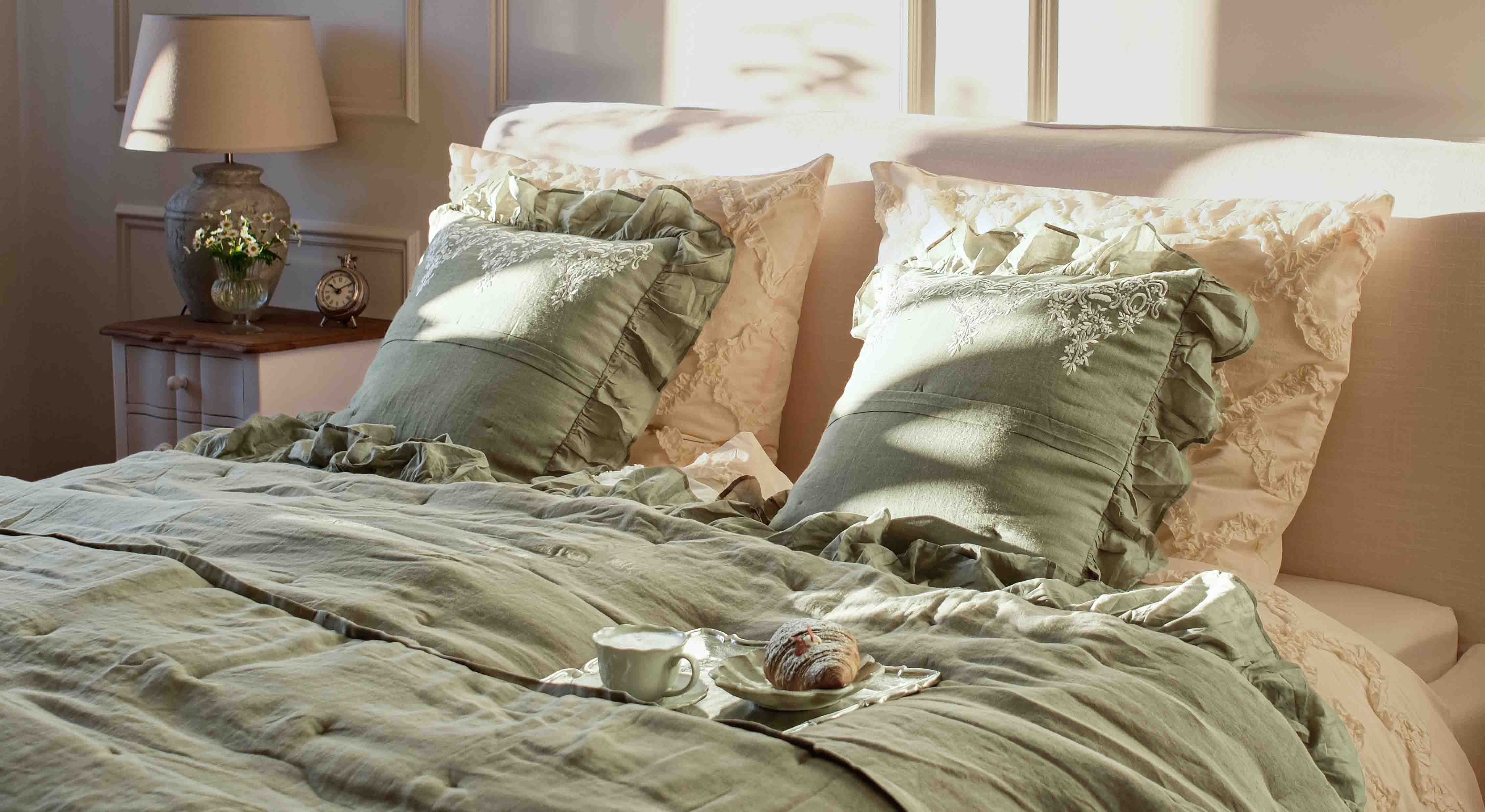 Biancheria da letto verde in lino con cuscini decorativi e federe crema in camera con lampada e orologio