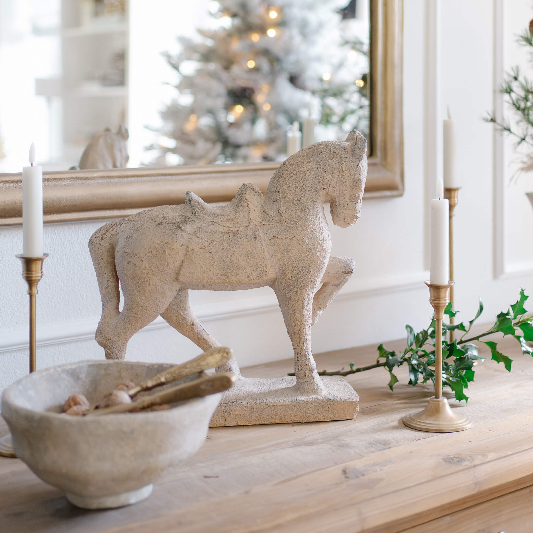 Scultura decorativa di cavallo in materiale pietroso beige su tavolo in legno con candele