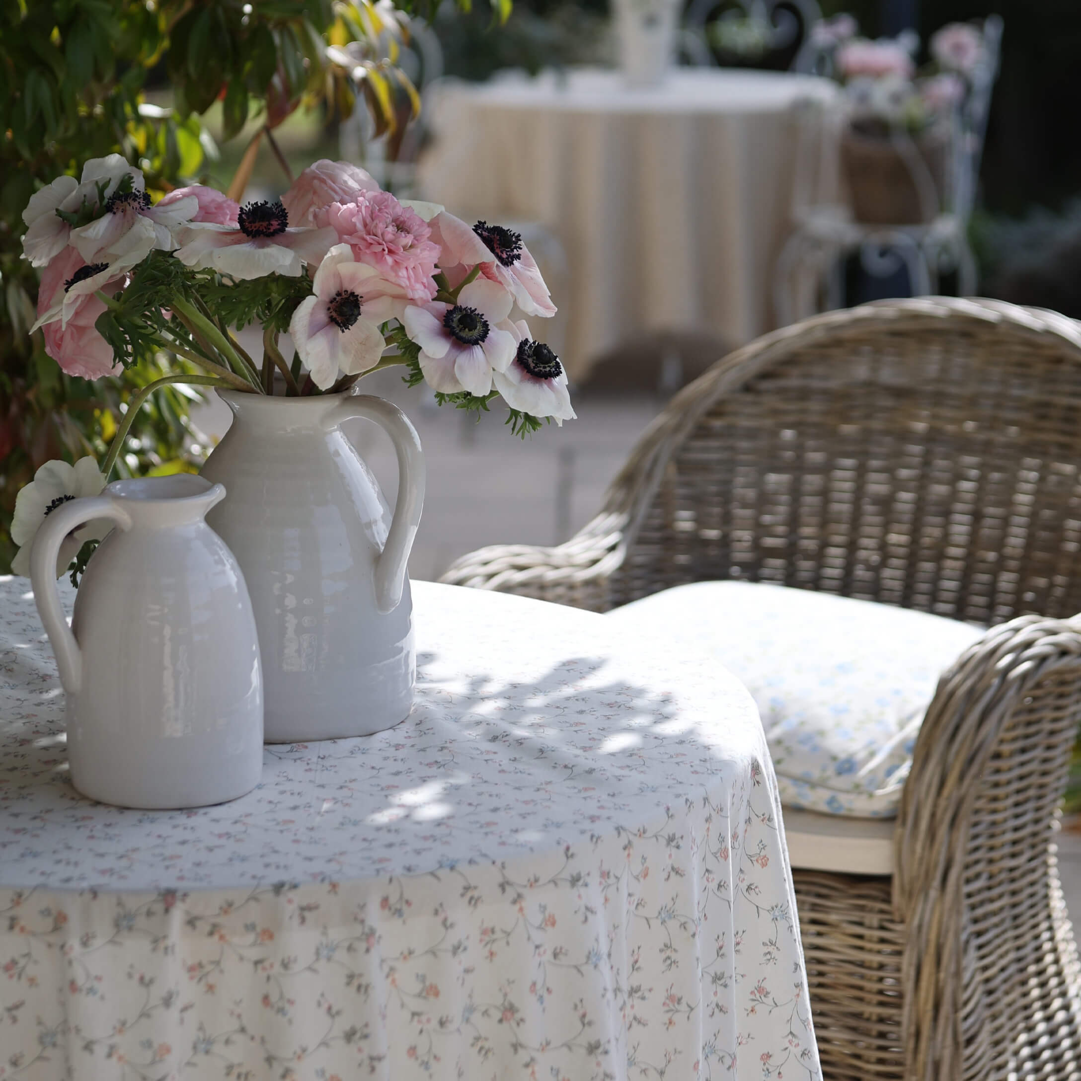 Brocche in ceramica bianca con fiori rosa e bianchi su tavolo con tovaglia floreale in giardino