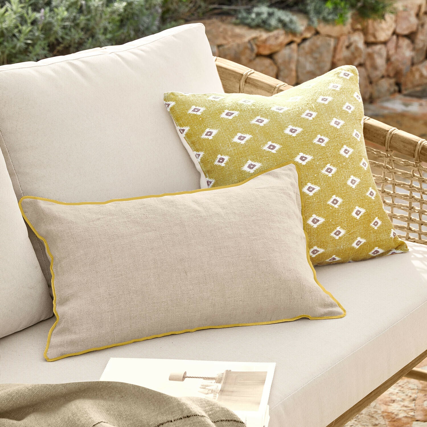 Coppia di copricuscini Brisalda Cuscino beige in lino con bordatura gialla e cuscino giallo con motivo bianco su divano da esterno chiaro
