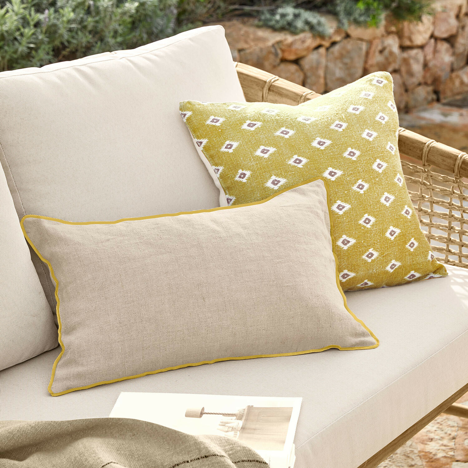 Coppia di copricuscini Brisalda Cuscino beige in lino con bordatura gialla e cuscino giallo con motivo bianco su divano da esterno chiaro