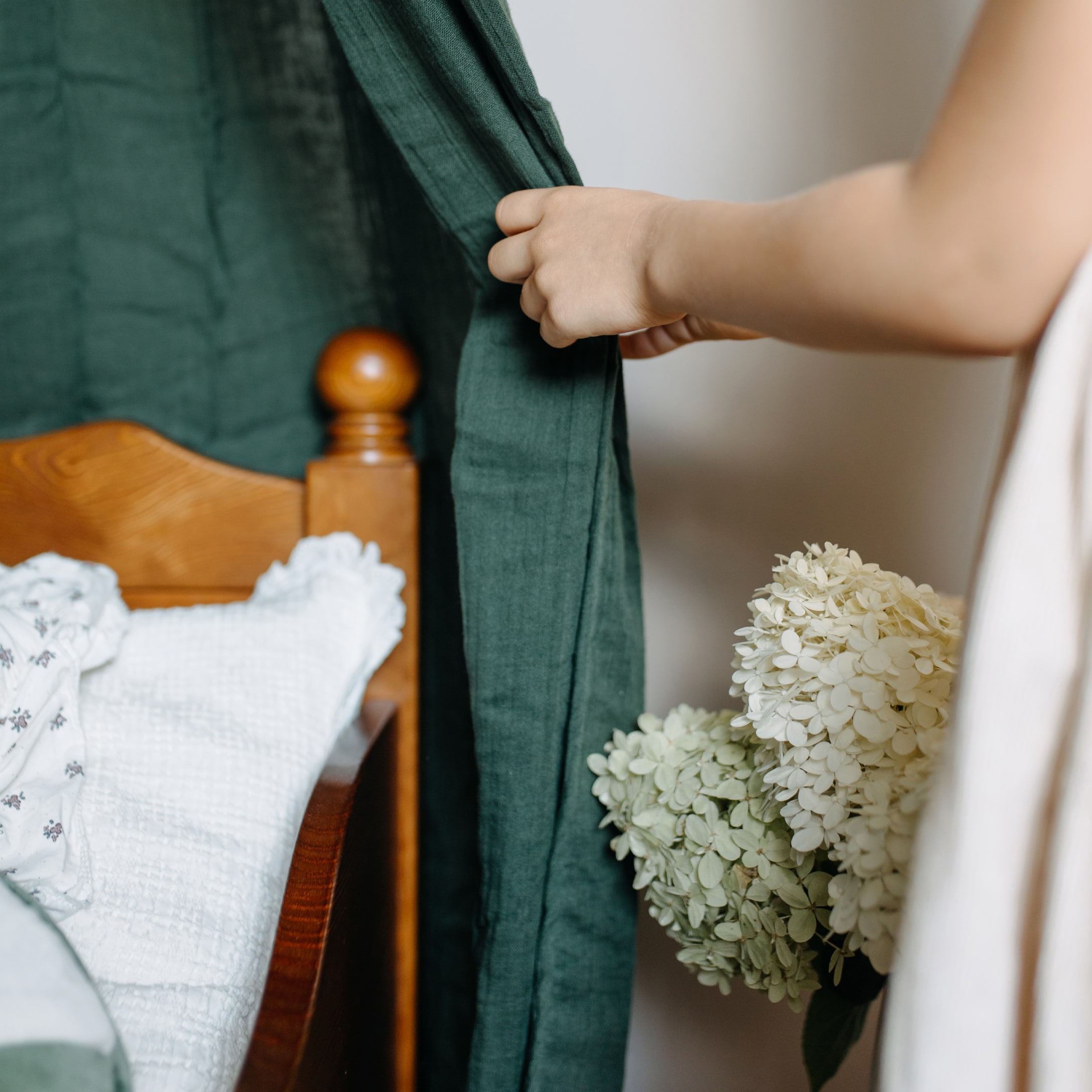 Bambino tiene tessuto verde accanto a un letto in legno con biancheria bianca e fiori di ortensia
