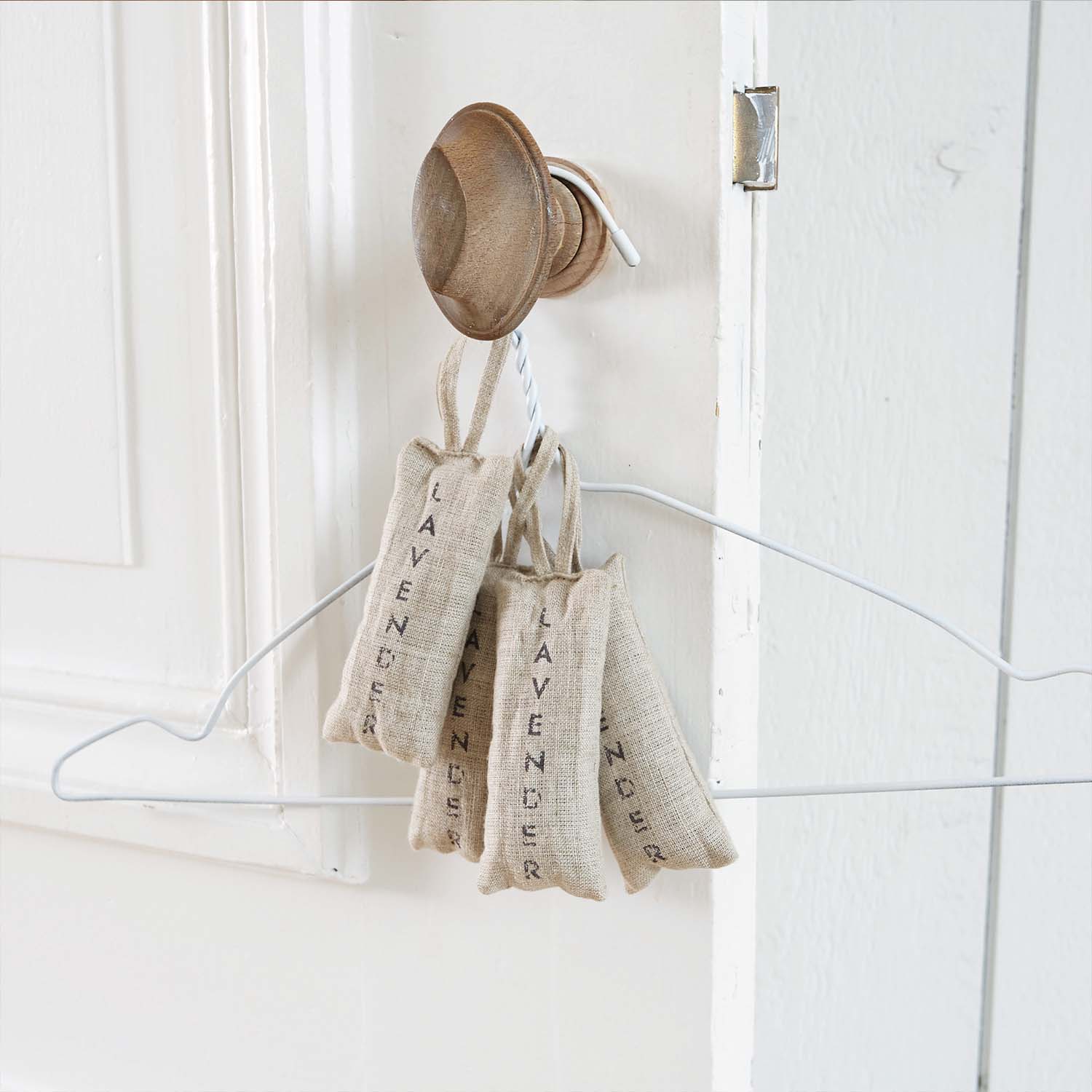 Sacchetti di lino naturale con lavanda appesi a un gancio in legno su porta bianca