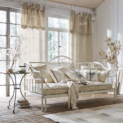 Divano in metallo bianco con cuscini beige e tende leggere in soggiorno rustico luminoso