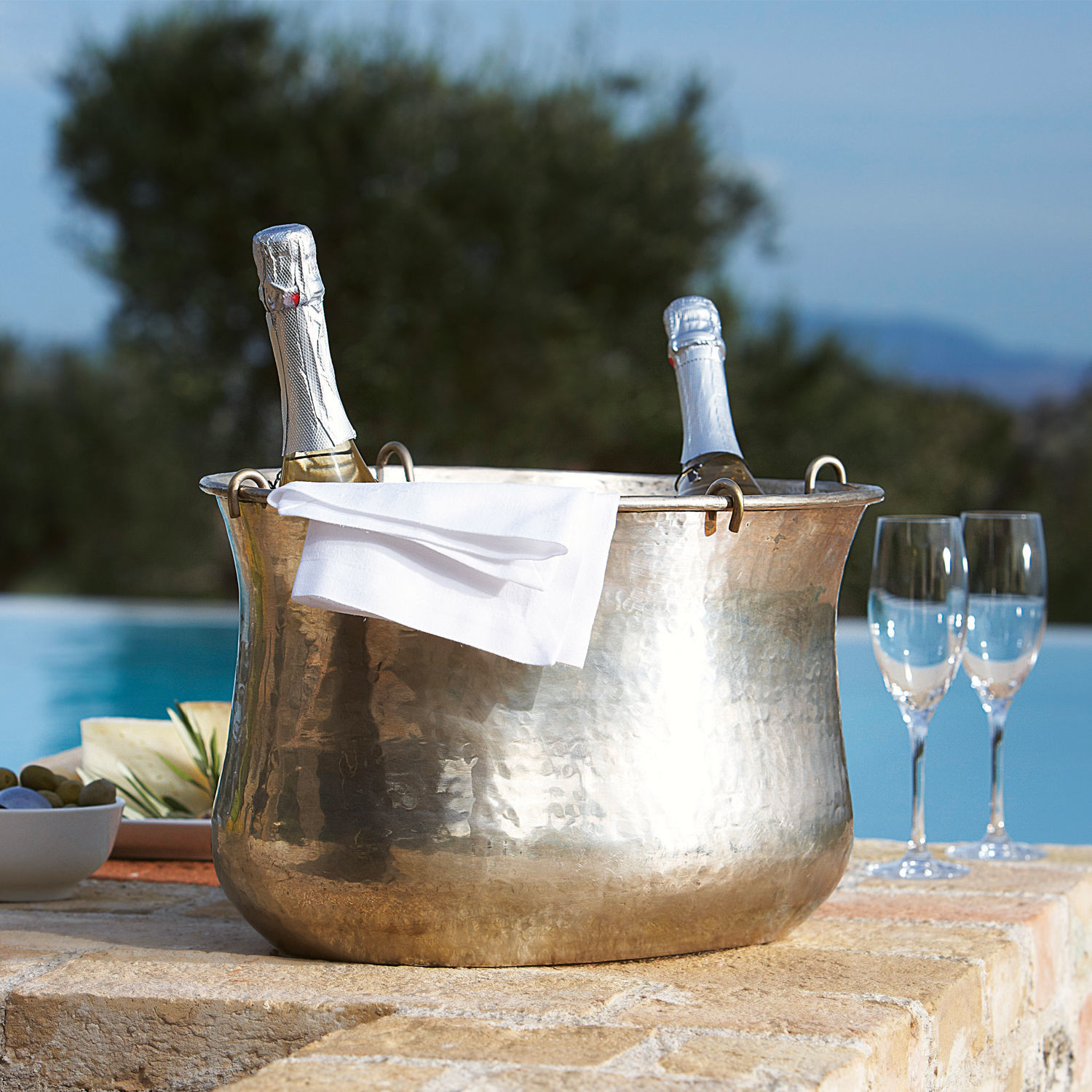 Secchiello del ghiaccio Montgomery Secchiello per ghiaccio in rame martellato con due bottiglie di champagne e tovagliolo bianco su terrazza