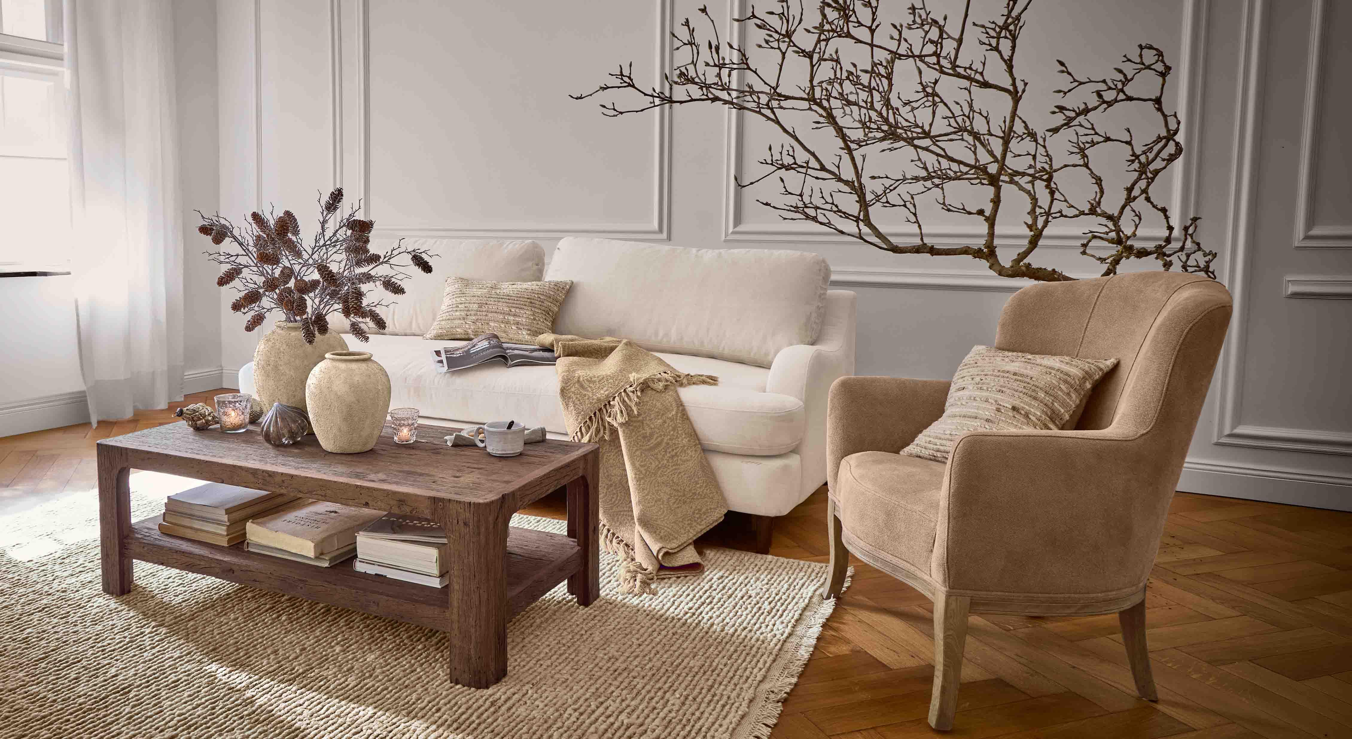 Soggiorno accogliente con divano beige, poltrona marrone e tavolino in legno su tappeto intrecciato