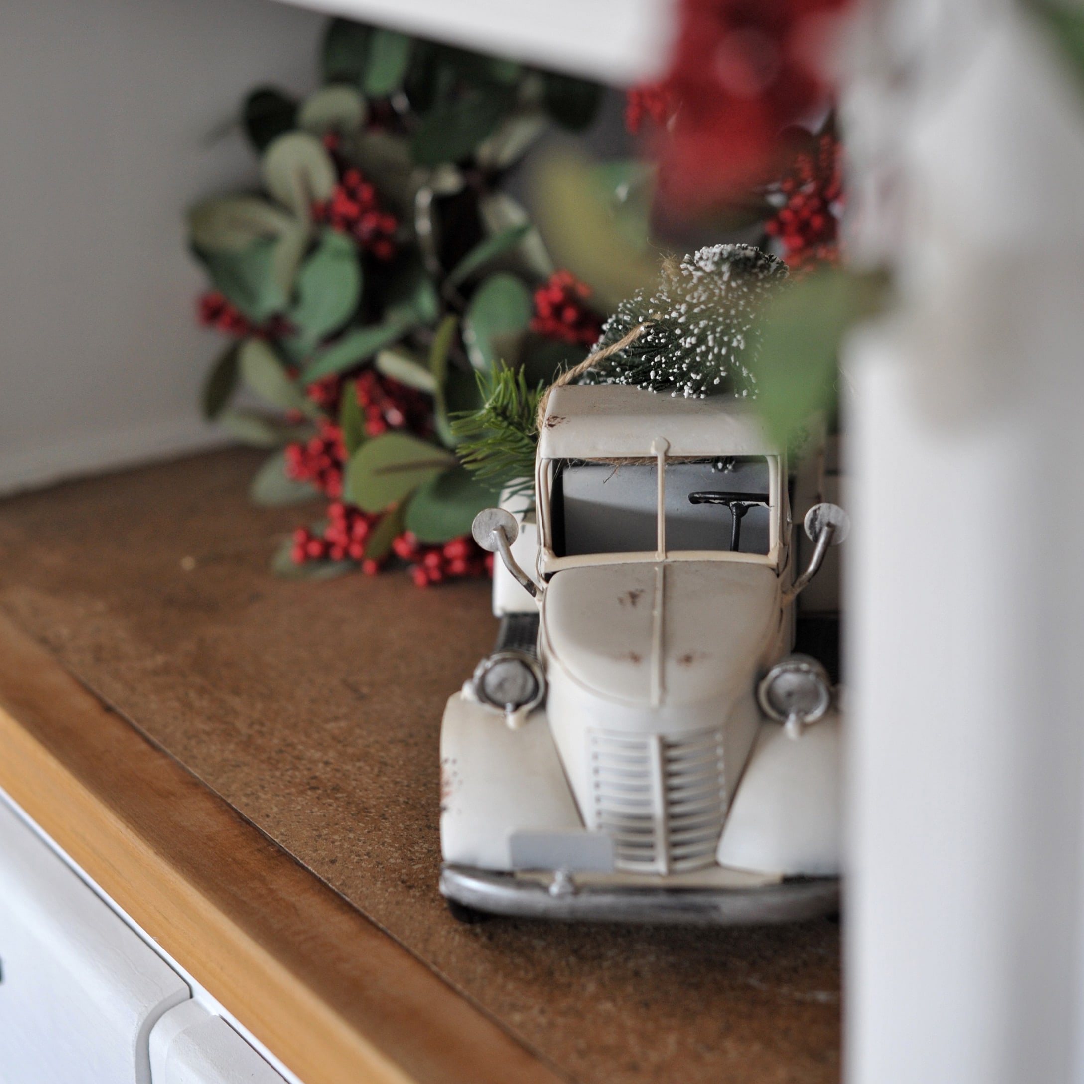 Modello di auto d'epoca in metallo bianco con decorazioni di foglie verdi e bacche rosse su piano in legno