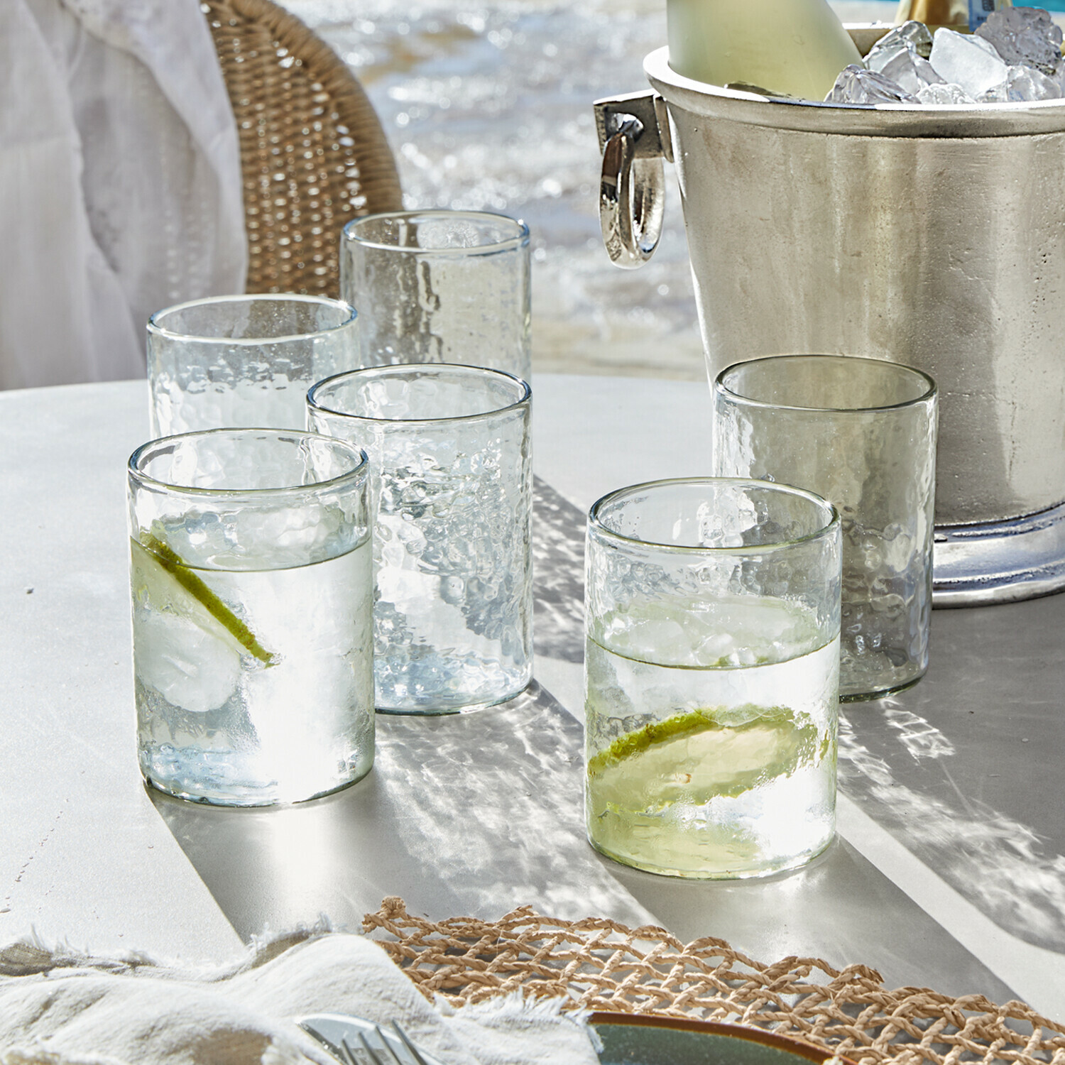 Bicchieri in vetro trasparente con texture, due con fette di lime e ghiaccio su tavolo bianco