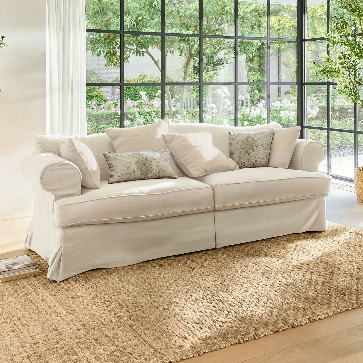 Divano Dawnhurst Divano beige in tessuto con cuscini decorativi su tappeto naturale in soggiorno luminoso con grandi finestre