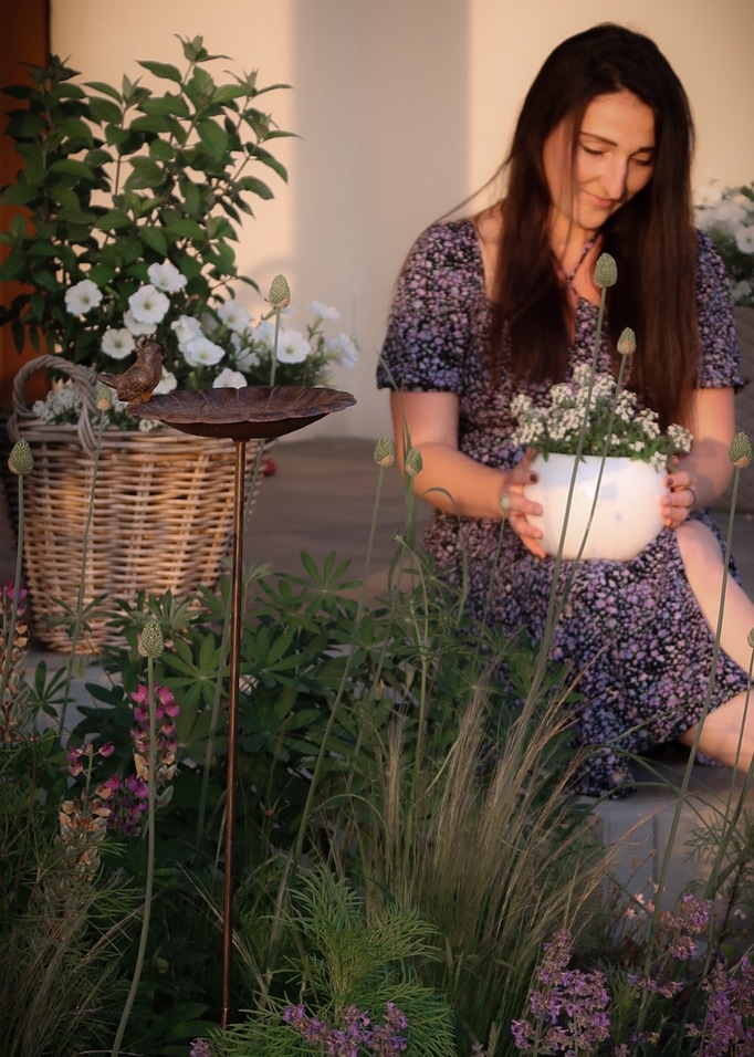 Abbeveratoio decorativo in metallo su piedistallo con uccello in giardino fiorito con donna in vestito