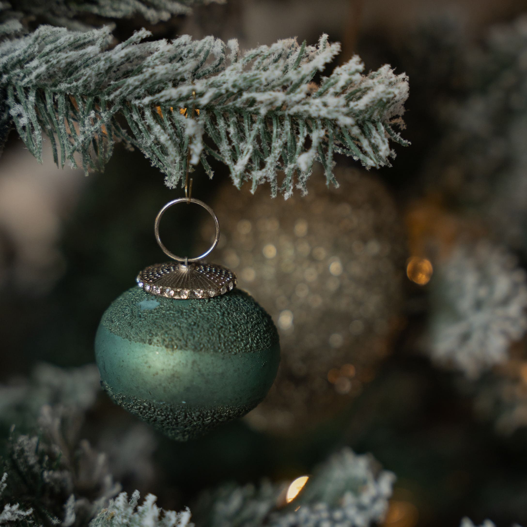 Pallina di Natale verde opaca con anello metallico appesa a ramo di abete innevato, decorazione festiva