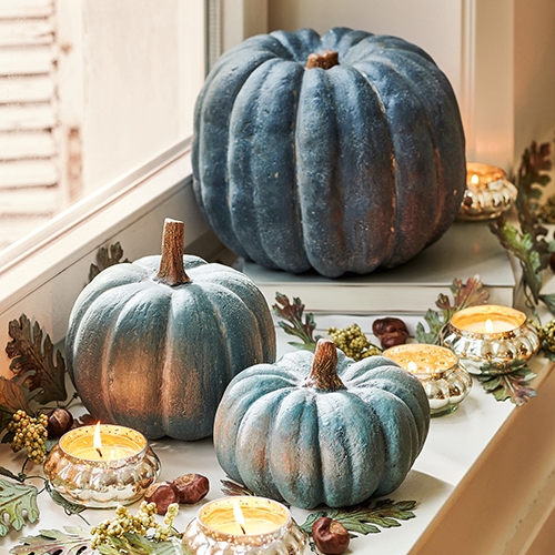 Zucca decorativa blu sul davanzale con candele accese e foglie autunnali