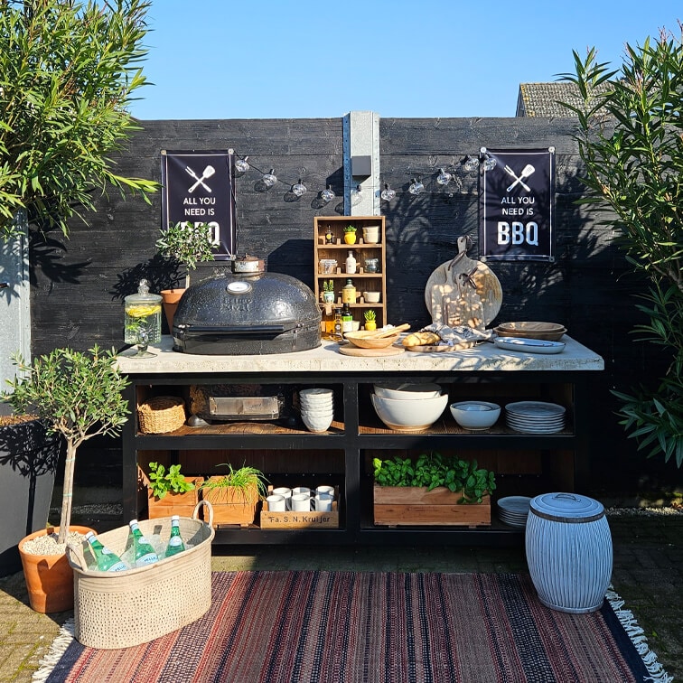 Area barbecue esterna con grill nero, piano bianco, piante in vaso e utensili da cucina