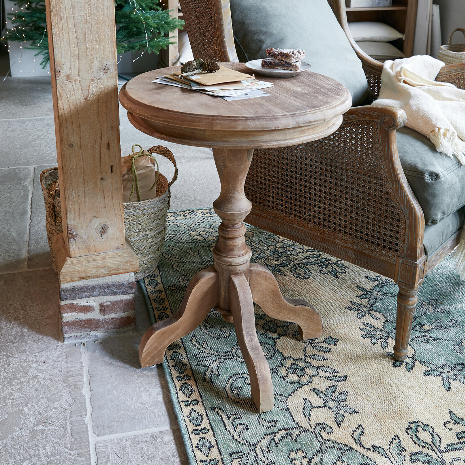 Tavolino di complemento Mengomeyen Tavolino rotondo in legno naturale accanto a una poltrona in vimini su tappeto decorato