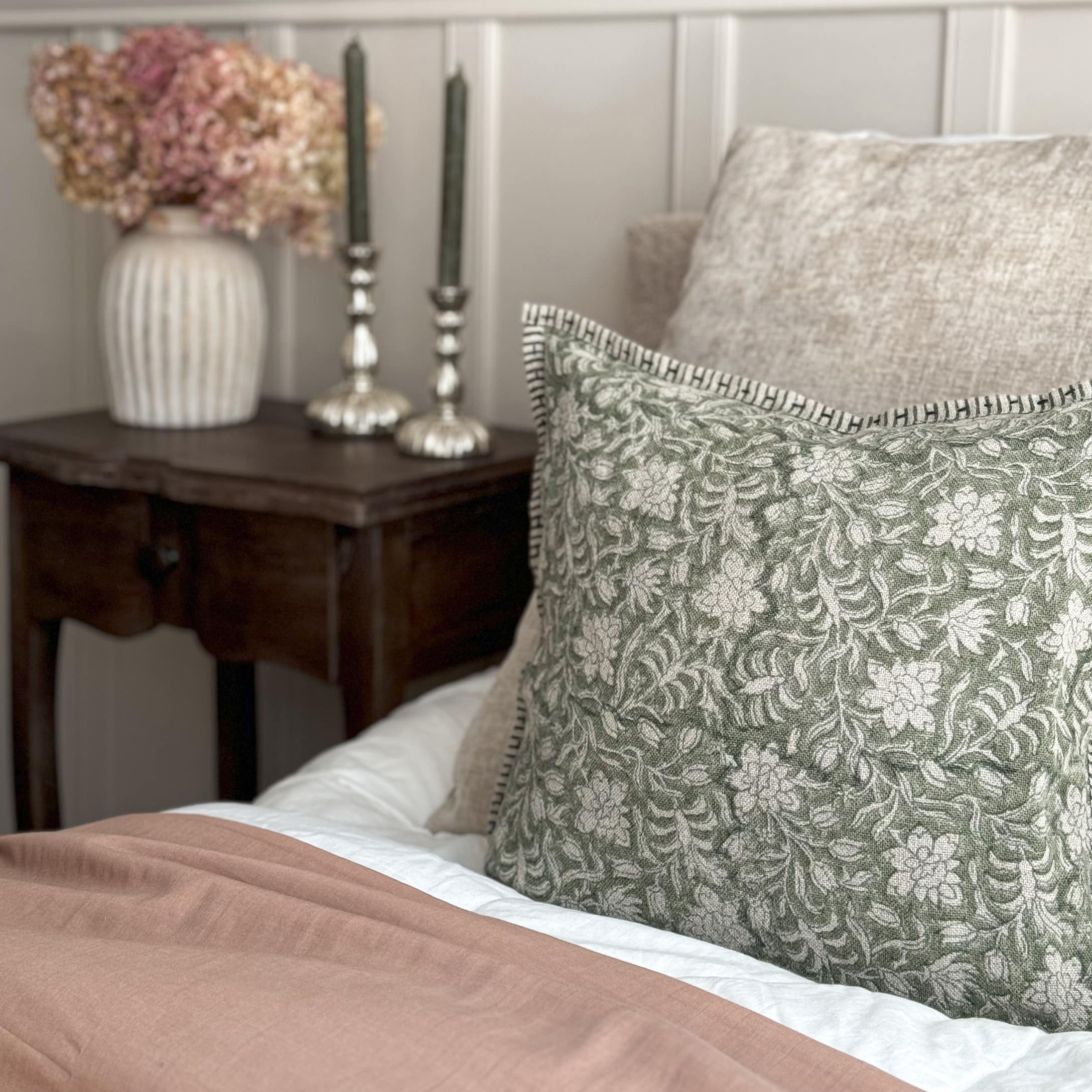 Cuscino decorativo verde con motivo floreale su tessuto beige su letto in stile vintage
