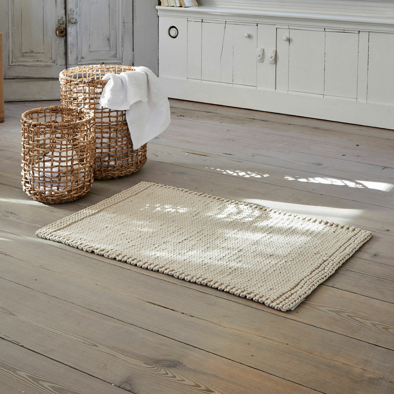 Scendibagno Carsen Tappeto beige in cotone su pavimento in legno con cesti di vimini per riporre