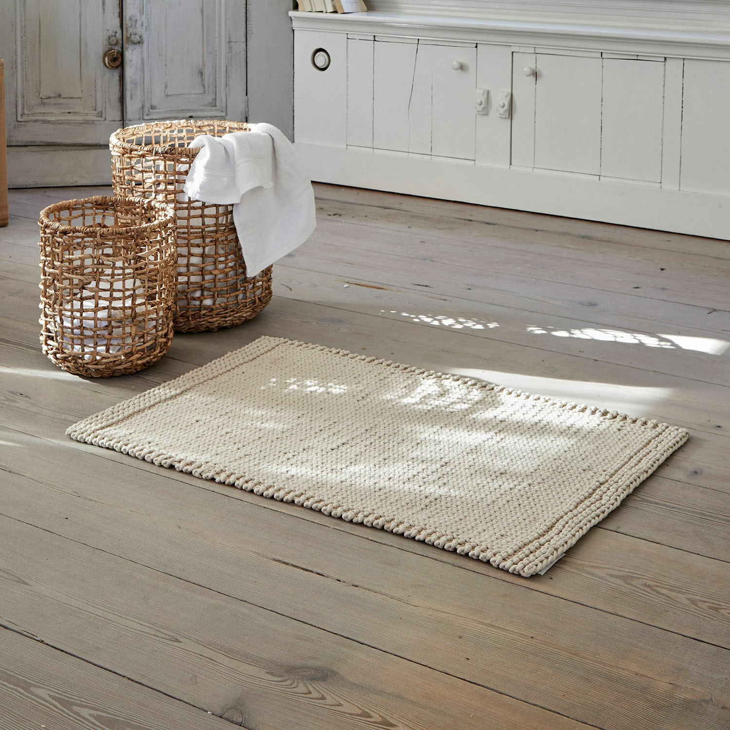 Scendibagno Carsen Tappeto beige in cotone su pavimento in legno con cesti di vimini per riporre