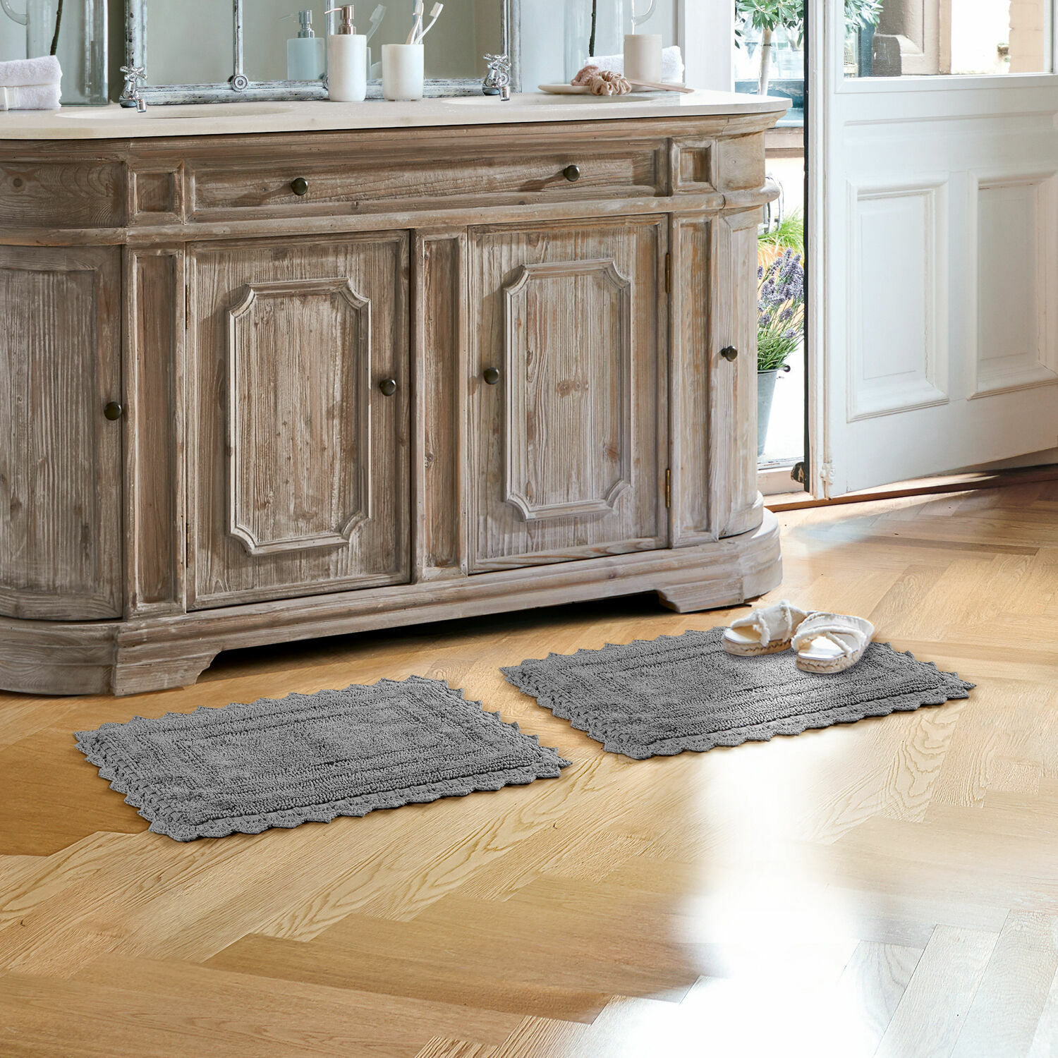Scendibagno Yalexir Tappeti da bagno grigi in cotone su pavimento in legno chiaro davanti a mobile rustico con lavabo