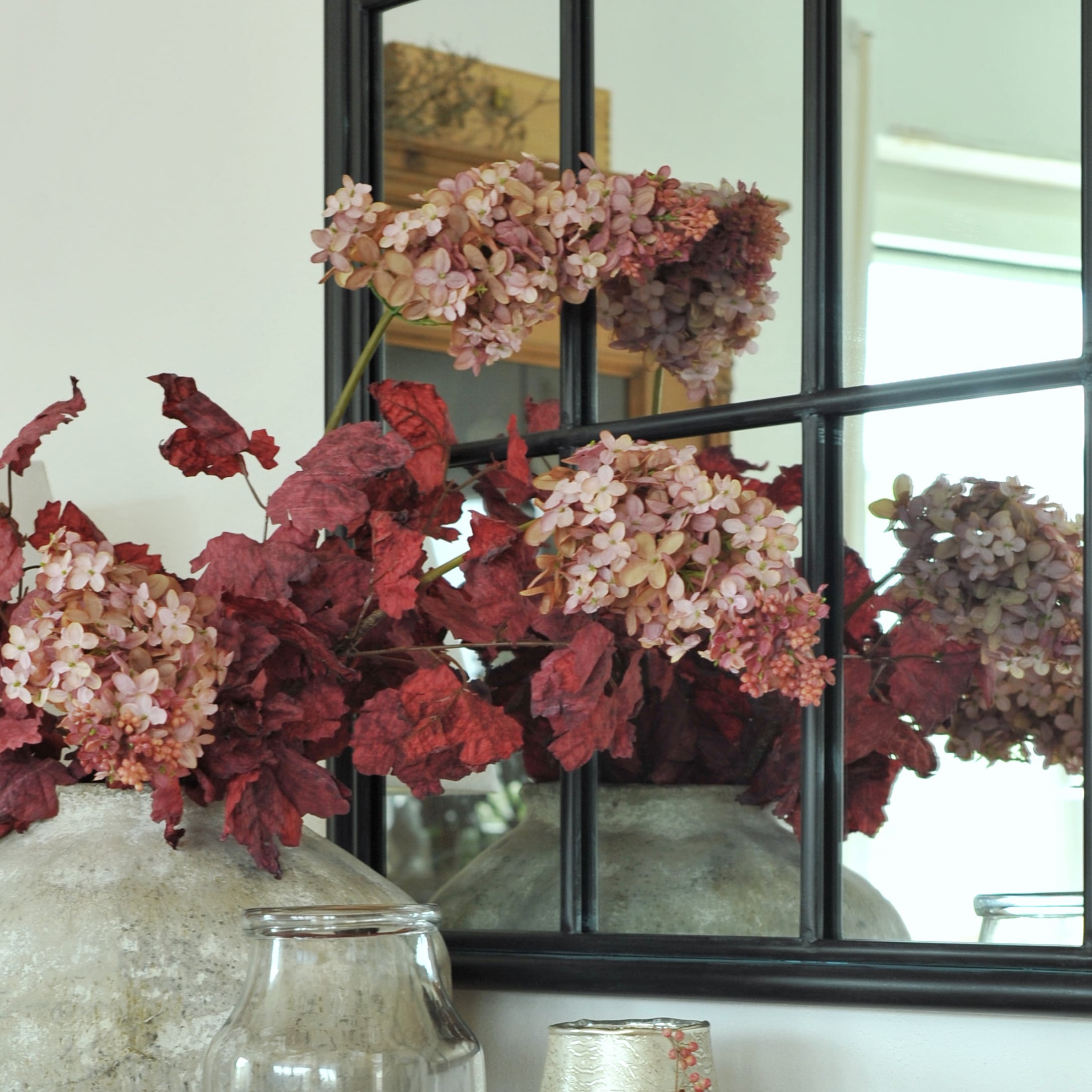 Vaso decorativo in pietra con foglie rosse e fiori rosa davanti a uno specchio nero