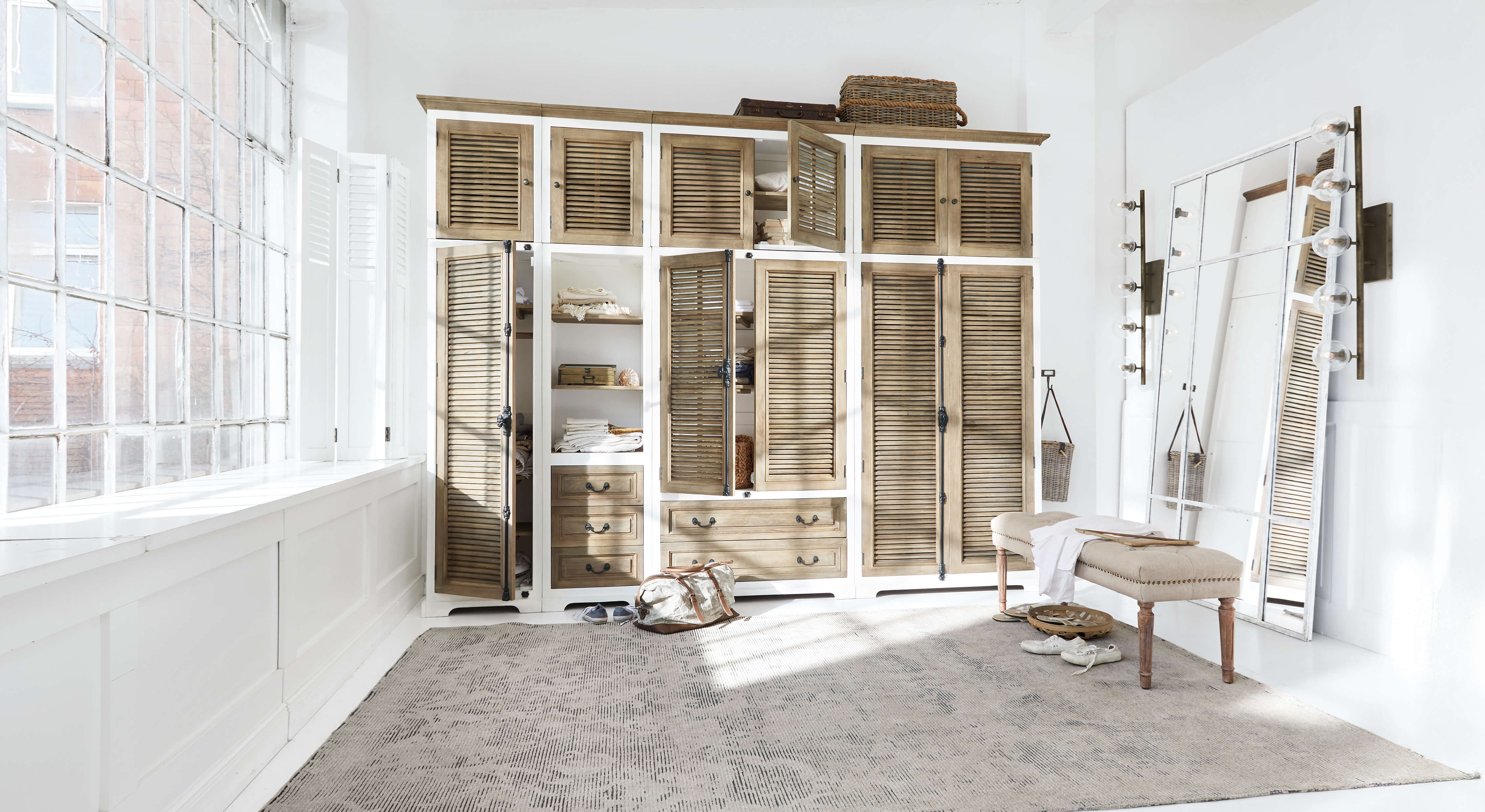 Ampio armadio in legno bianco e naturale con ante a persiana e grande specchio in stanza luminosa