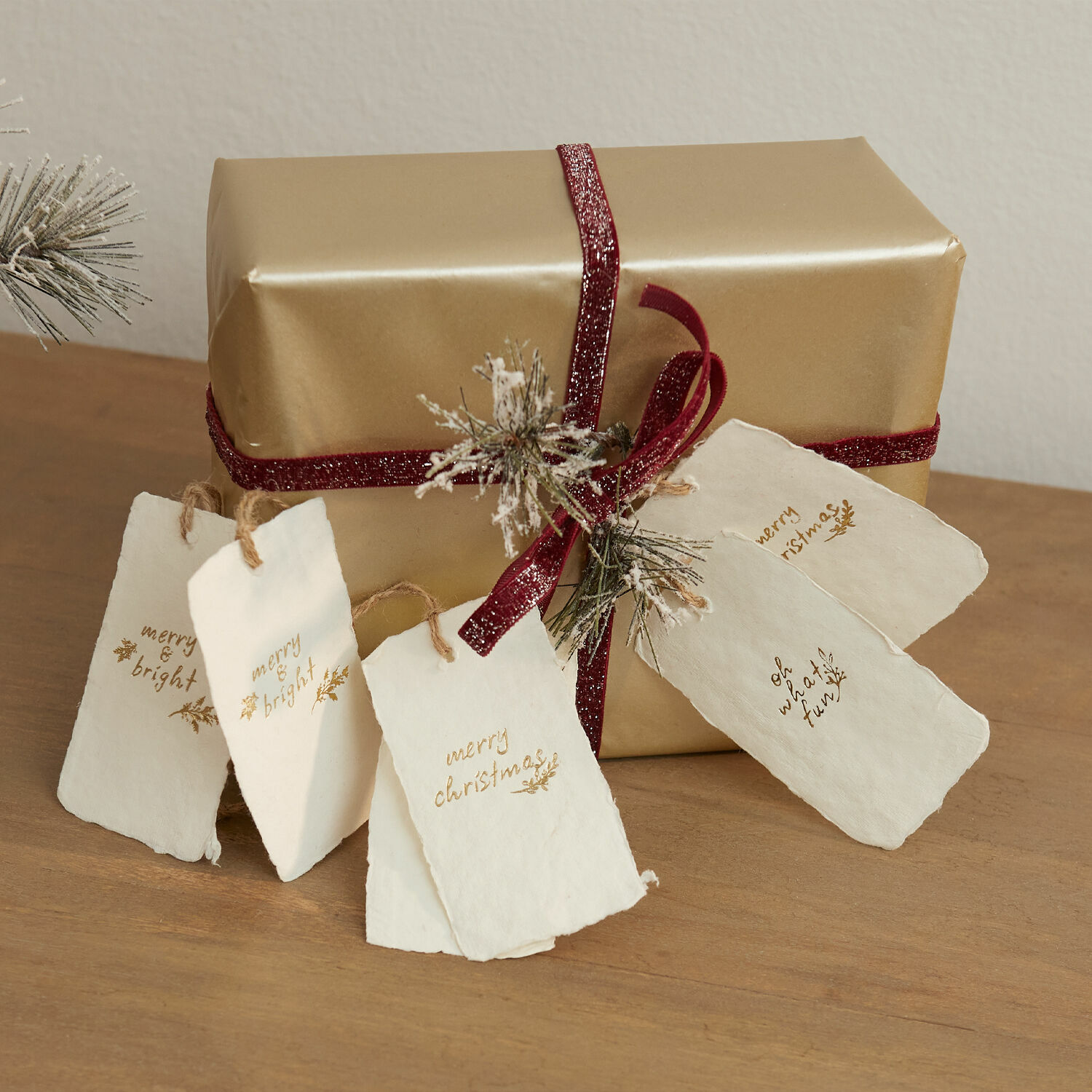 Set di 6 cartellini da regalo Aamira Regalo dorato con nastro bordeaux e etichette di carta bianche natalizie su tavolo in legno