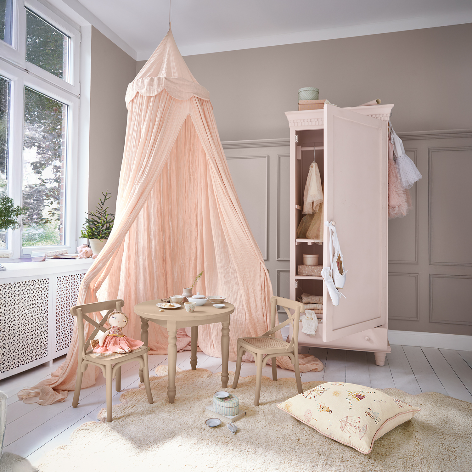 Accogliente cameretta con baldacchino rosa, tavolo e sedie in legno, armadio rosa aperto con vestiti