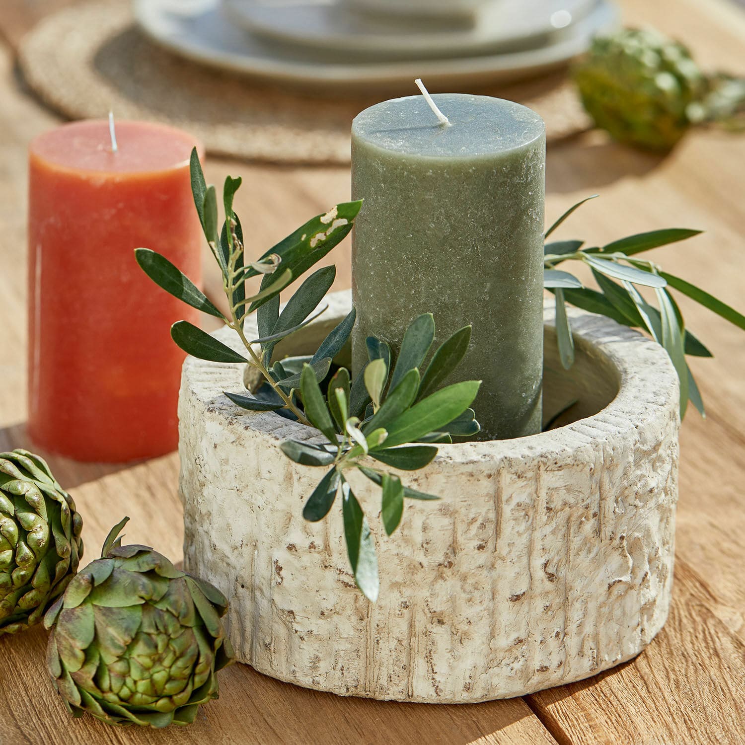 Ciotola Continas Portacandele rotondo in pietra beige con candela verde e decorazione di foglie su tavolo in legno