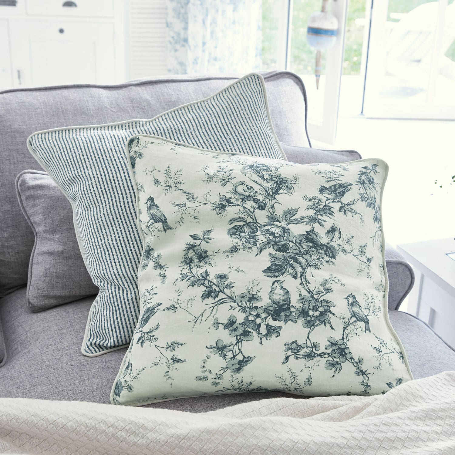 Coppia di cuscini Emilie Cuscino decorativo reversibile in cotone con motivi floreali e righe blu su divano grigio