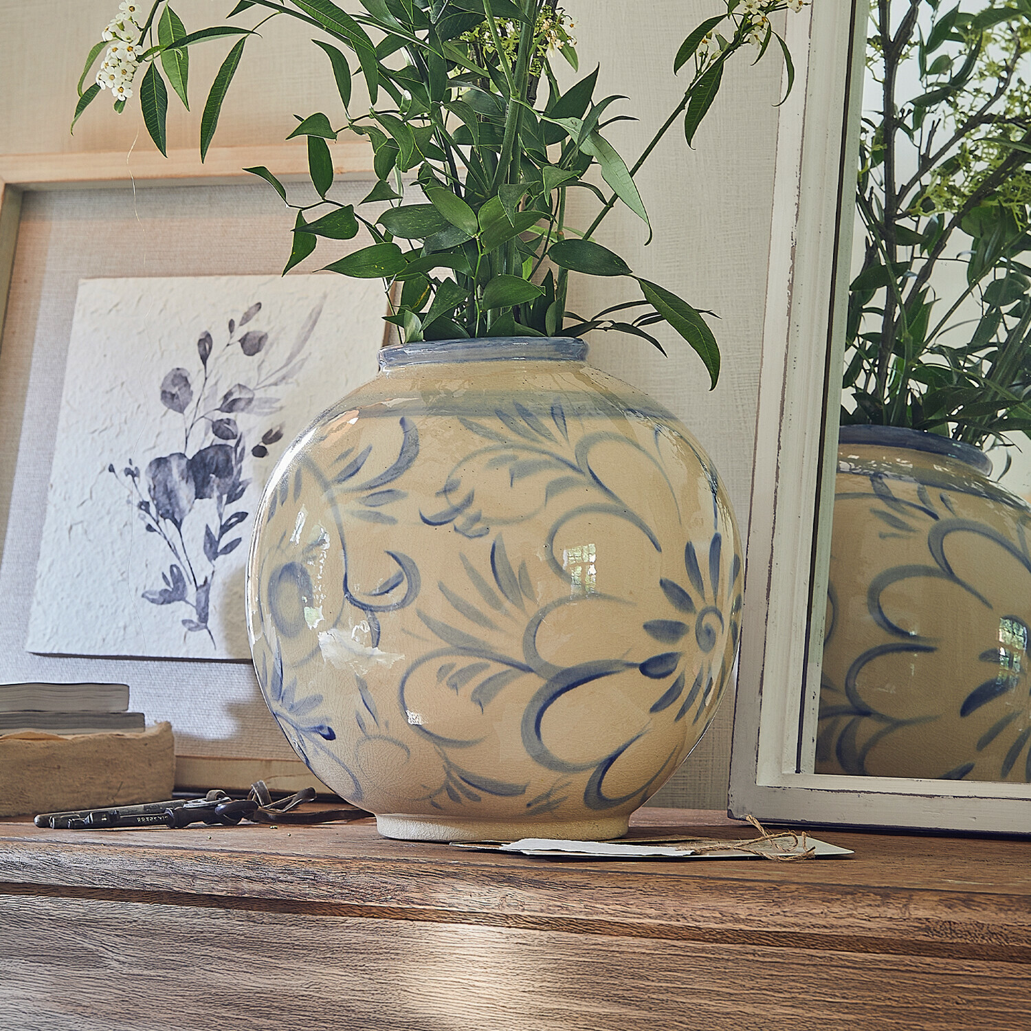 Vaso Oviren Vaso rotondo in ceramica beige con motivo floreale blu su tavolo in legno con foglie verdi