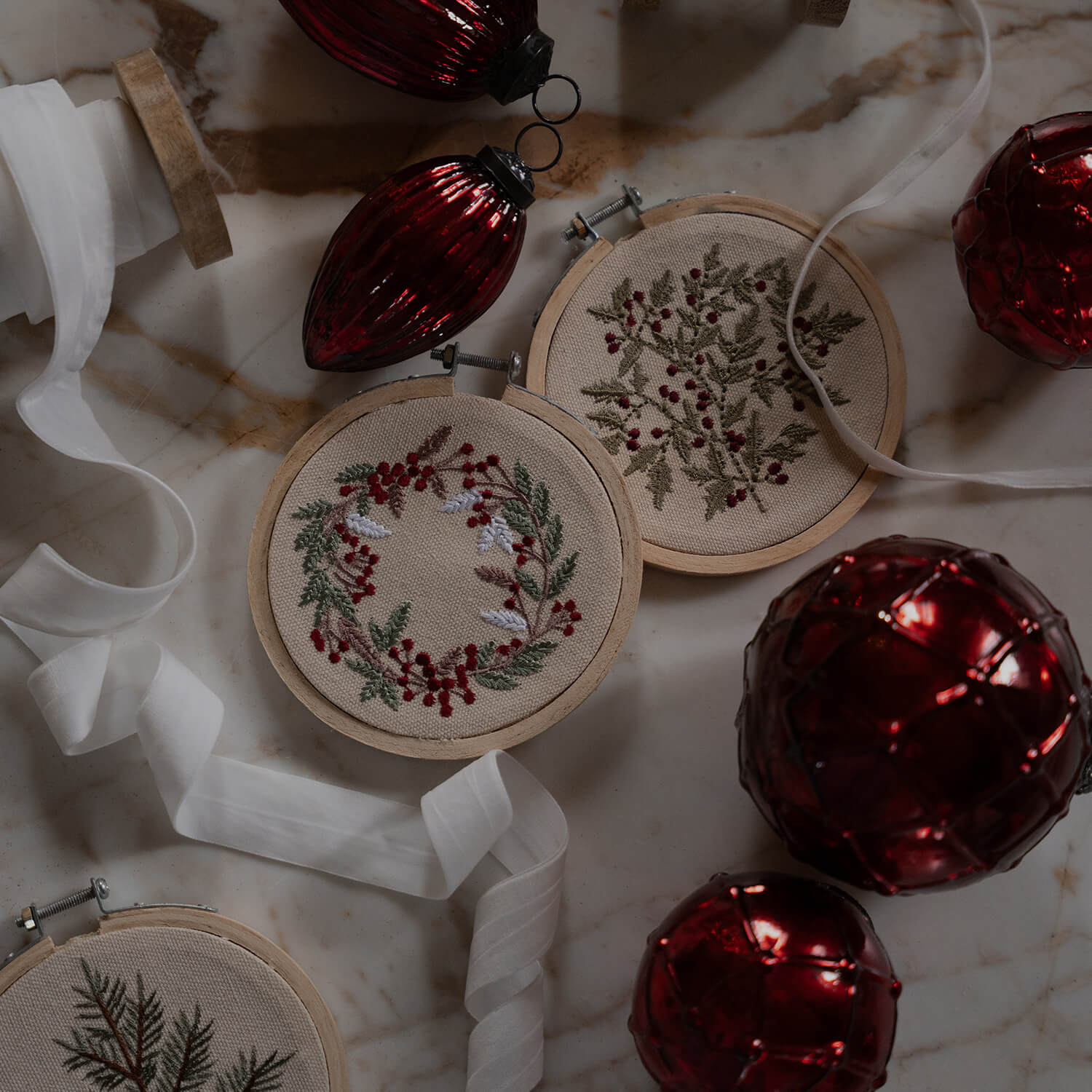 Decorazioni natalizie con motivi vegetali ricamati su tessuto beige e palline rosse lucide