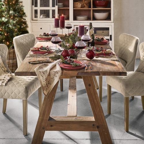 Tavolo in legno con sedie beige trapuntate e decorazioni natalizie con candele rosse e bicchieri di vino
