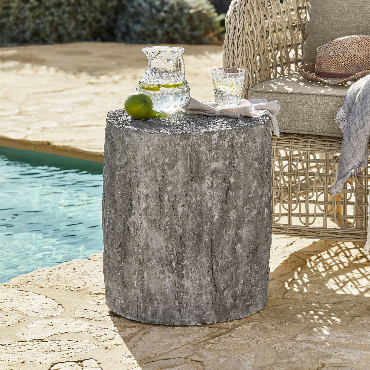 Tavolino grigio in cemento con texture legno accanto a poltrona in vimini vicino alla piscina