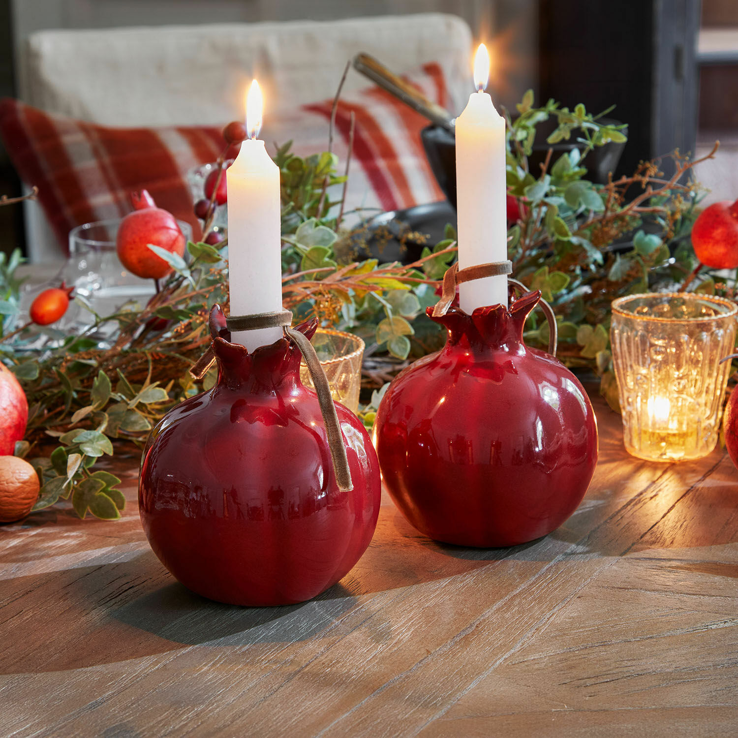 Coppia di portacandele Karidah Due candelieri in ceramica rossa a forma di melograno con candele bianche su tavolo in legno decorato