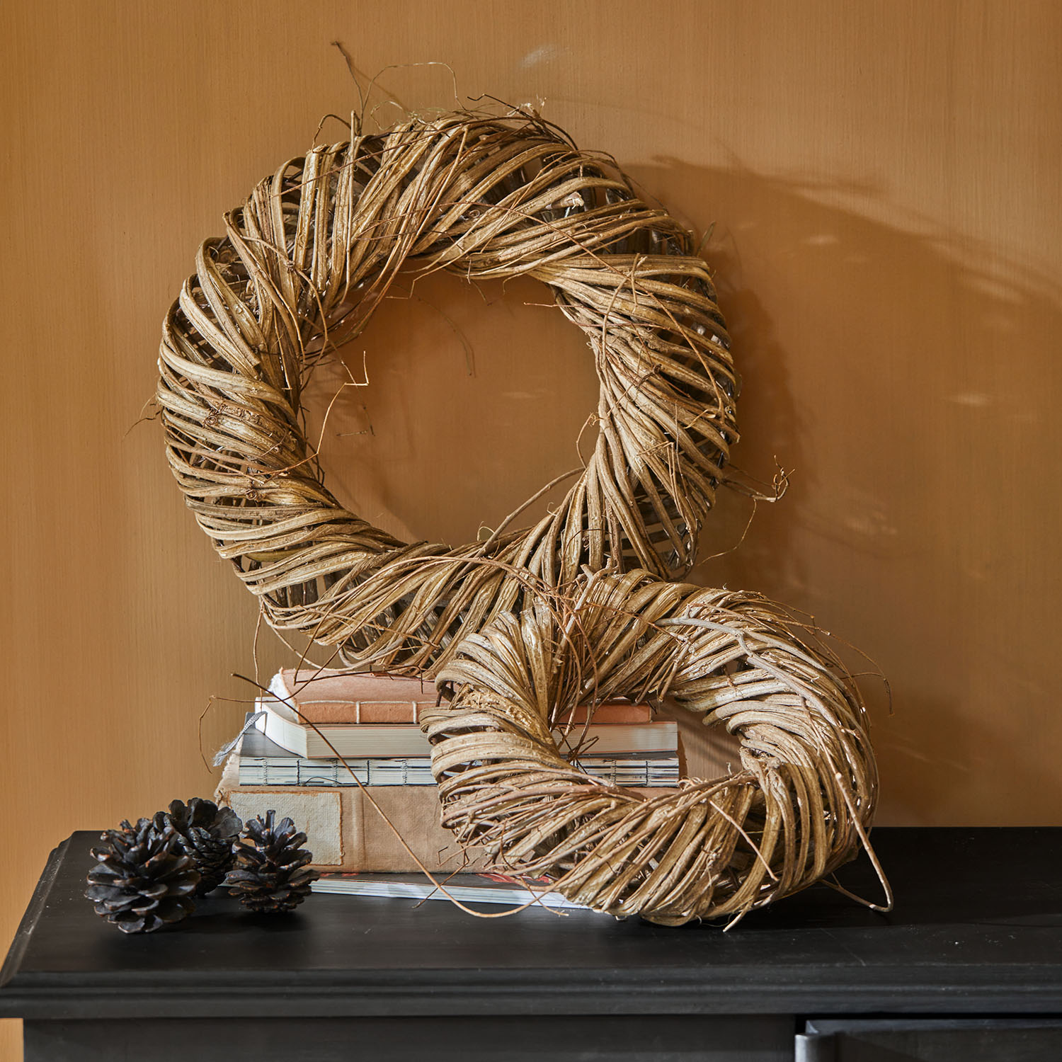Corona decorativa in vimini naturale marrone su superficie nera con pigne decorative