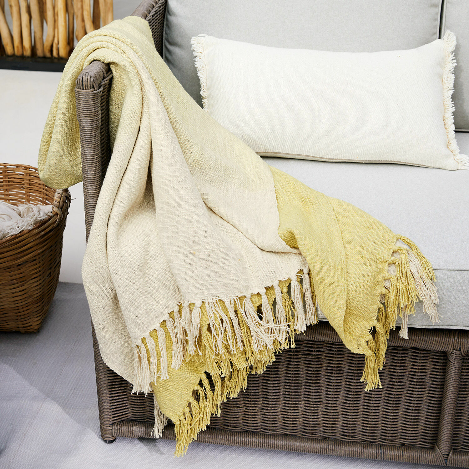 Plaid Aurice Coperta bicolore in cotone crema e giallo con frange su divano in rattan grigio