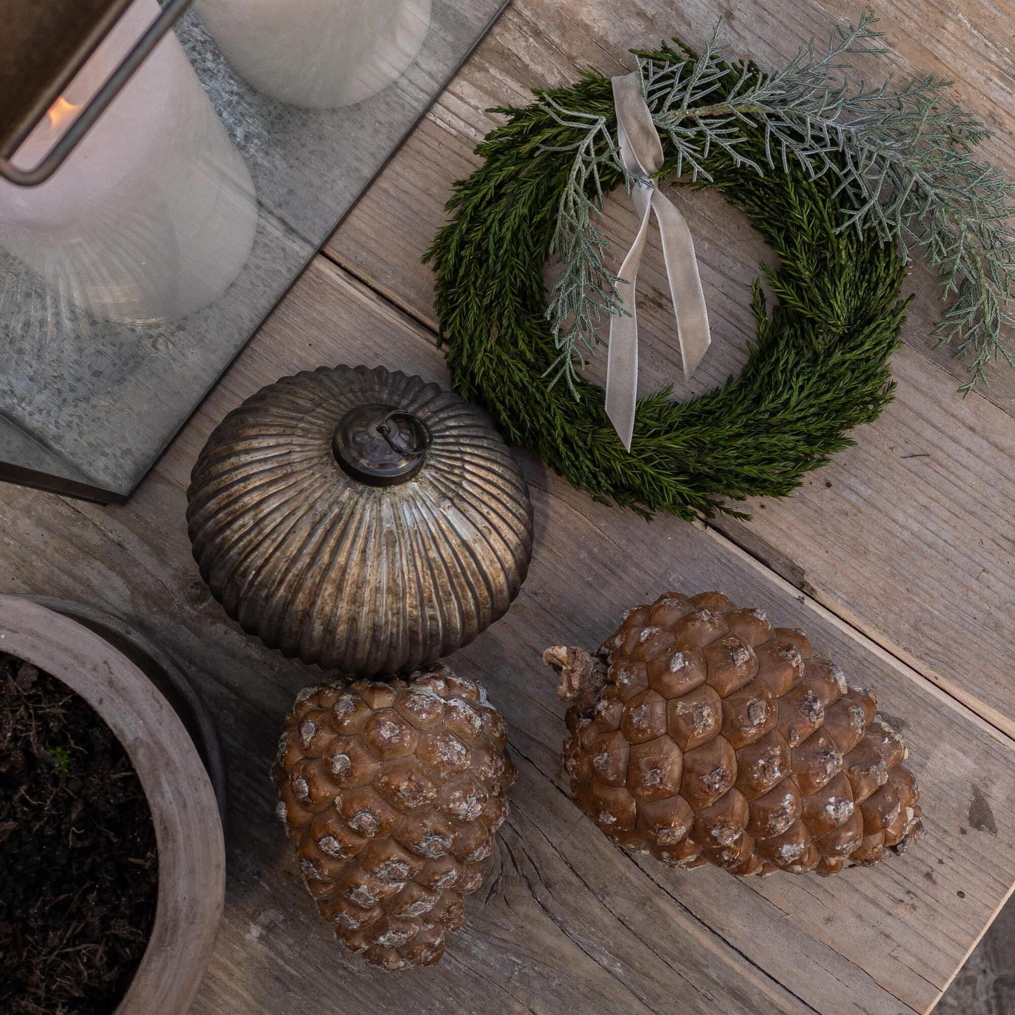 Corona decorativa di rami verdi con nastro grigio e pigne naturali su tavolo in legno