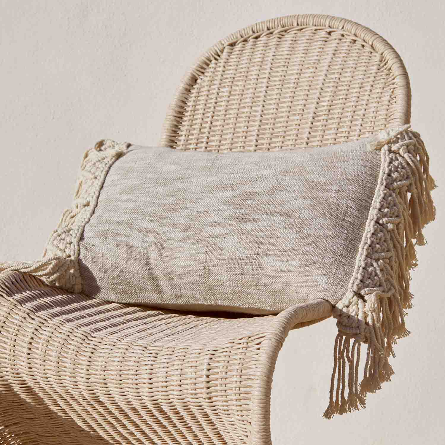Cuscino decorativo beige con frange su sedia in vimini, materiale naturale, stile boho